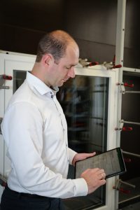 technischer Leiter hält vor dem Fensterprüfstand ein Tablet in der Hand